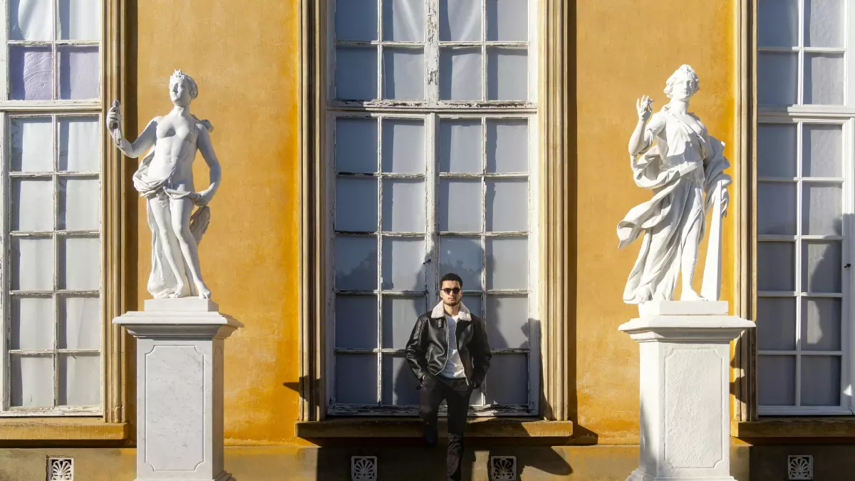 A person wearing a black coat is sitting on a bench in front of two white statues in a park.