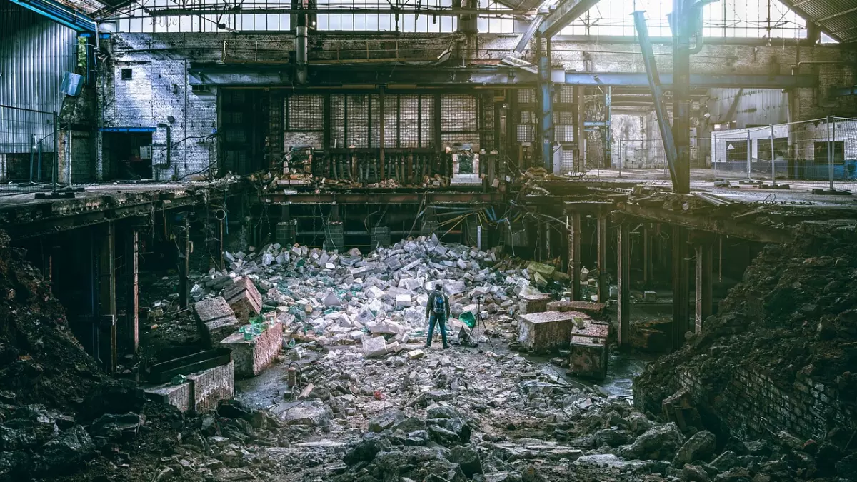 A large, collapsed structure with debris scattered throughout. A lone figure is standing in the center of the frame, making the image appear even more dramatic.