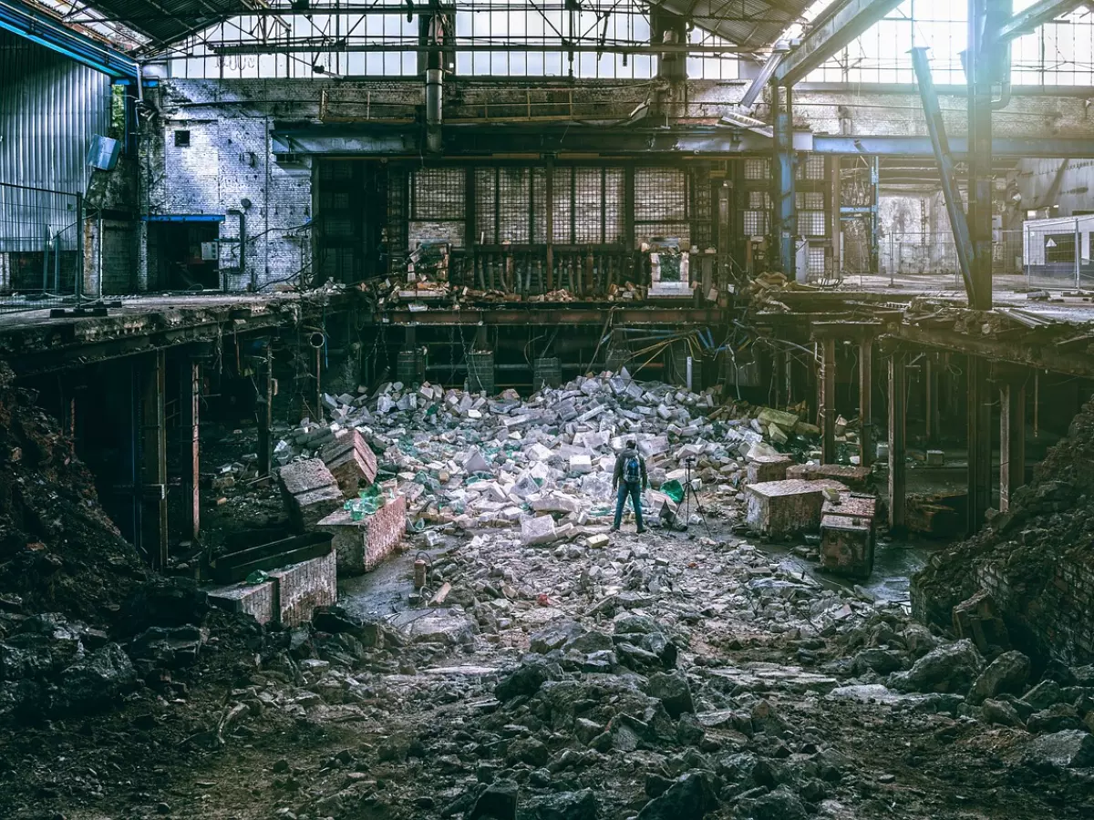 A large, collapsed structure with debris scattered throughout. A lone figure is standing in the center of the frame, making the image appear even more dramatic.