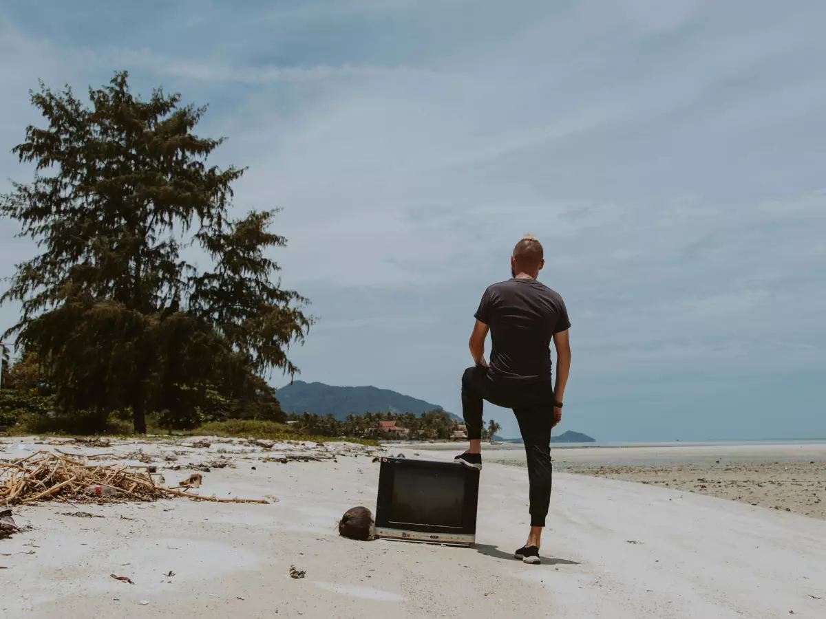 A man on a beach with a broken TV.