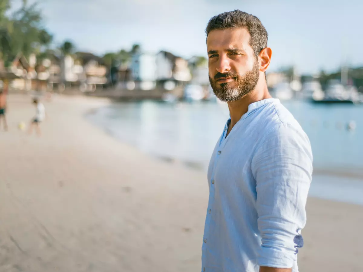 A man on a beach holding a smartphone. The background is blurred.