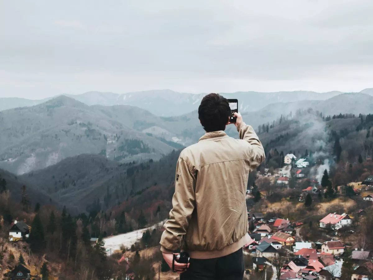 A person standing on a hill overlooking a valley and taking a picture with a phone.