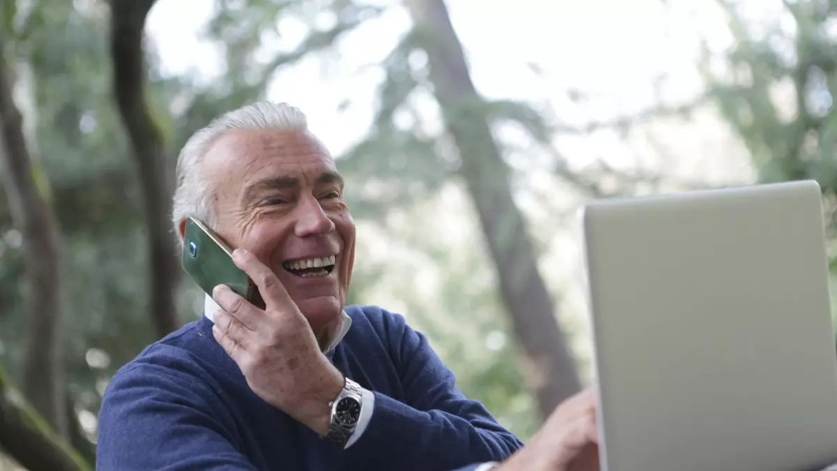 A man talking on the phone while working on a laptop in a park.