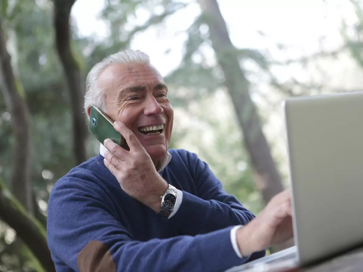 A man talking on the phone while working on a laptop in a park.