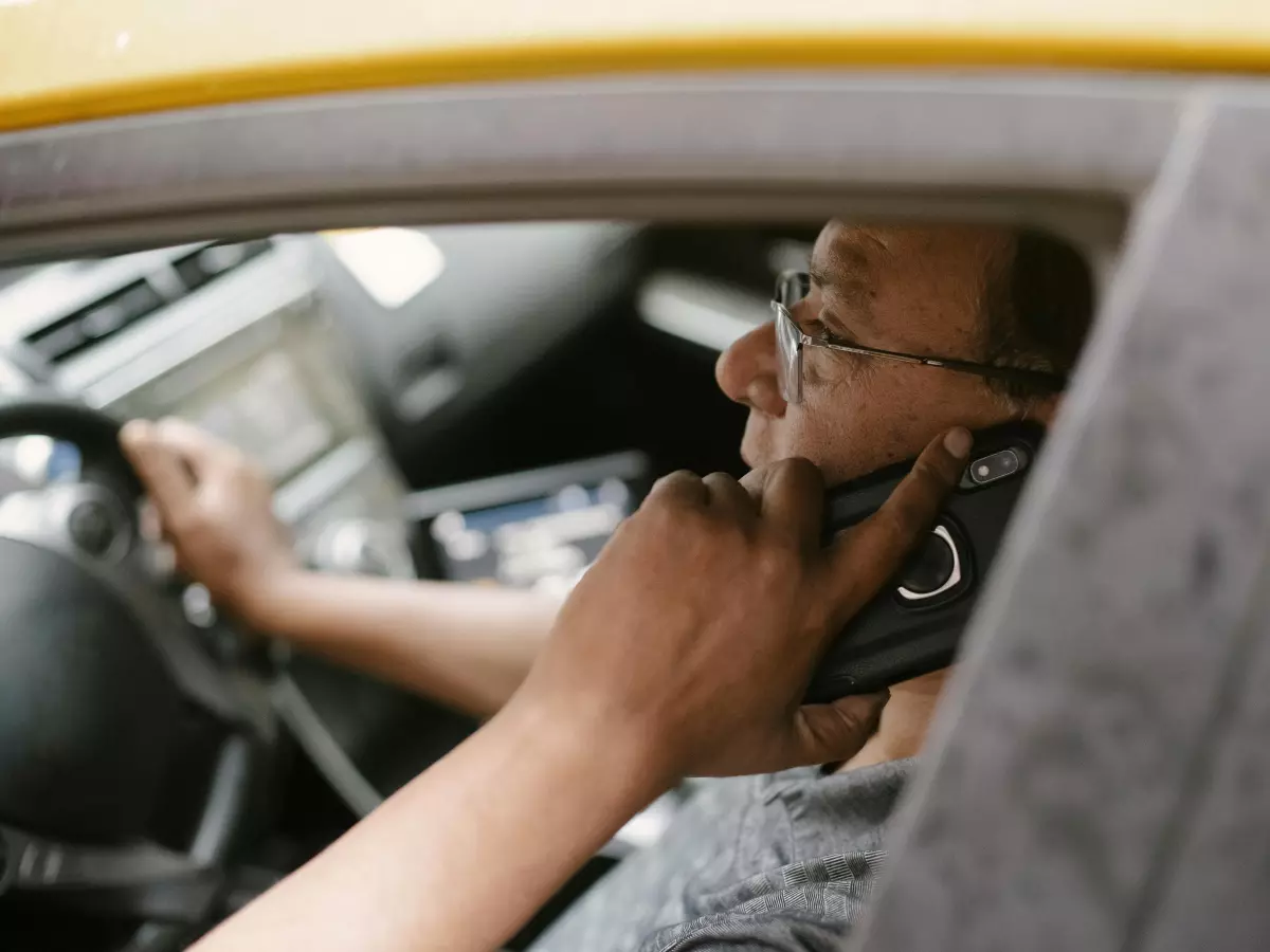 A man driving a yellow car with a phone to his ear.