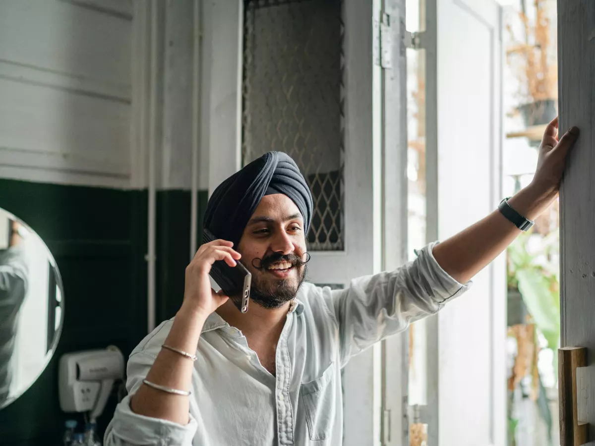 A man in a white shirt and turban is talking on his phone while standing in a doorway.