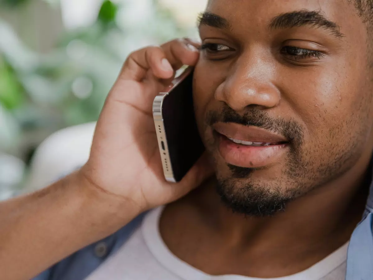 A close-up of a man talking on a smartphone. He is wearing a blue shirt and has a beard.