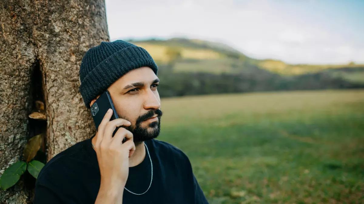 A man talking on his smartphone while leaning against a tree