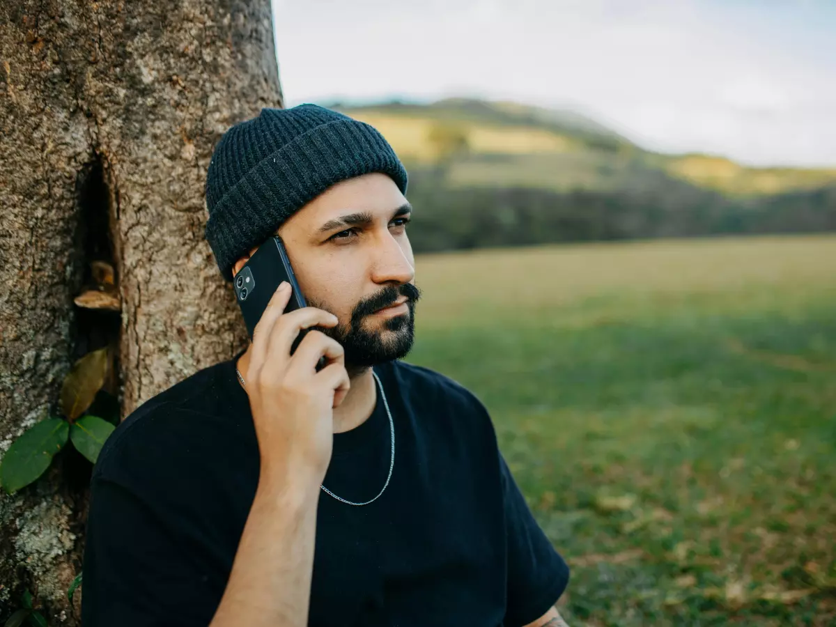 A man talking on his smartphone while leaning against a tree