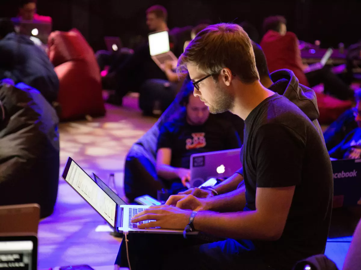 A group of people are working on their laptops in a room. They are sitting on bean bags and using their devices.