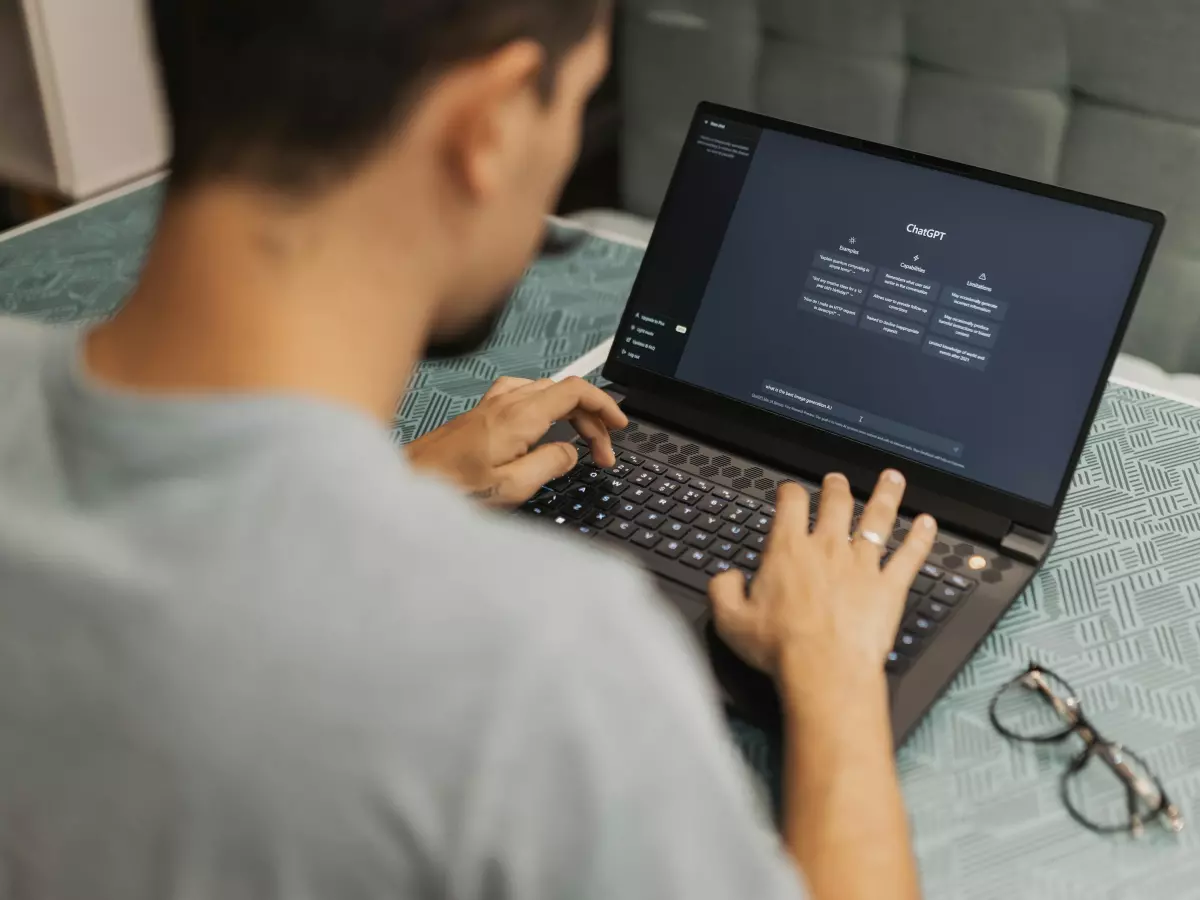 A person is typing on a laptop, sitting at a desk. The laptop screen is showing a document with text on it.