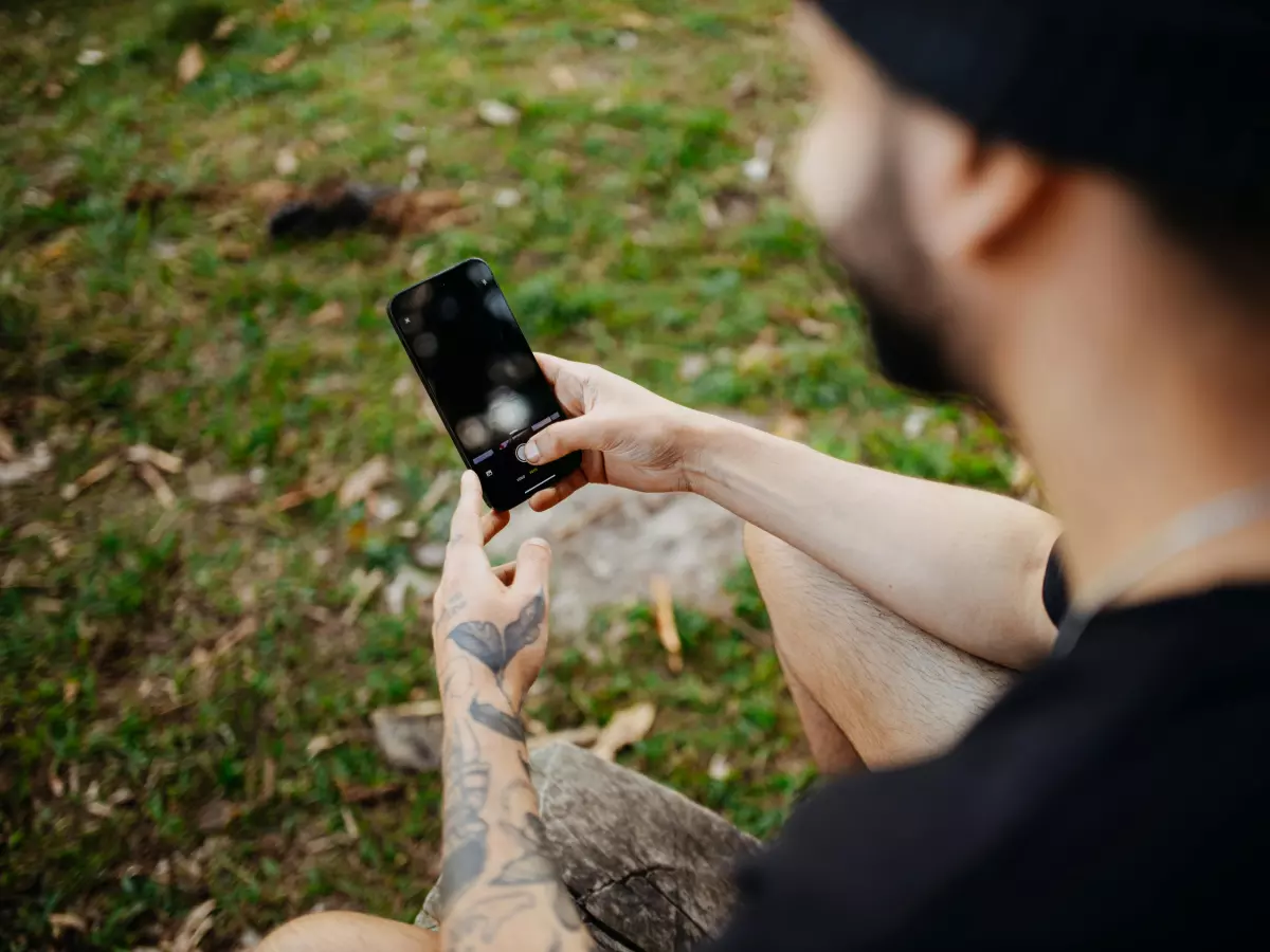 A man with tattoos on his arm is using a smartphone outdoors.