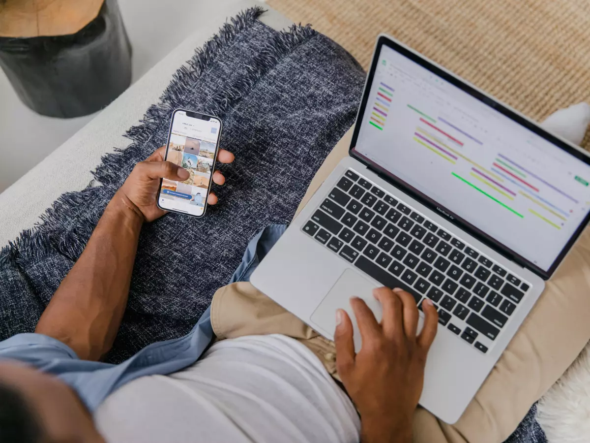 A person is sitting on a couch and using a smartphone and a laptop.