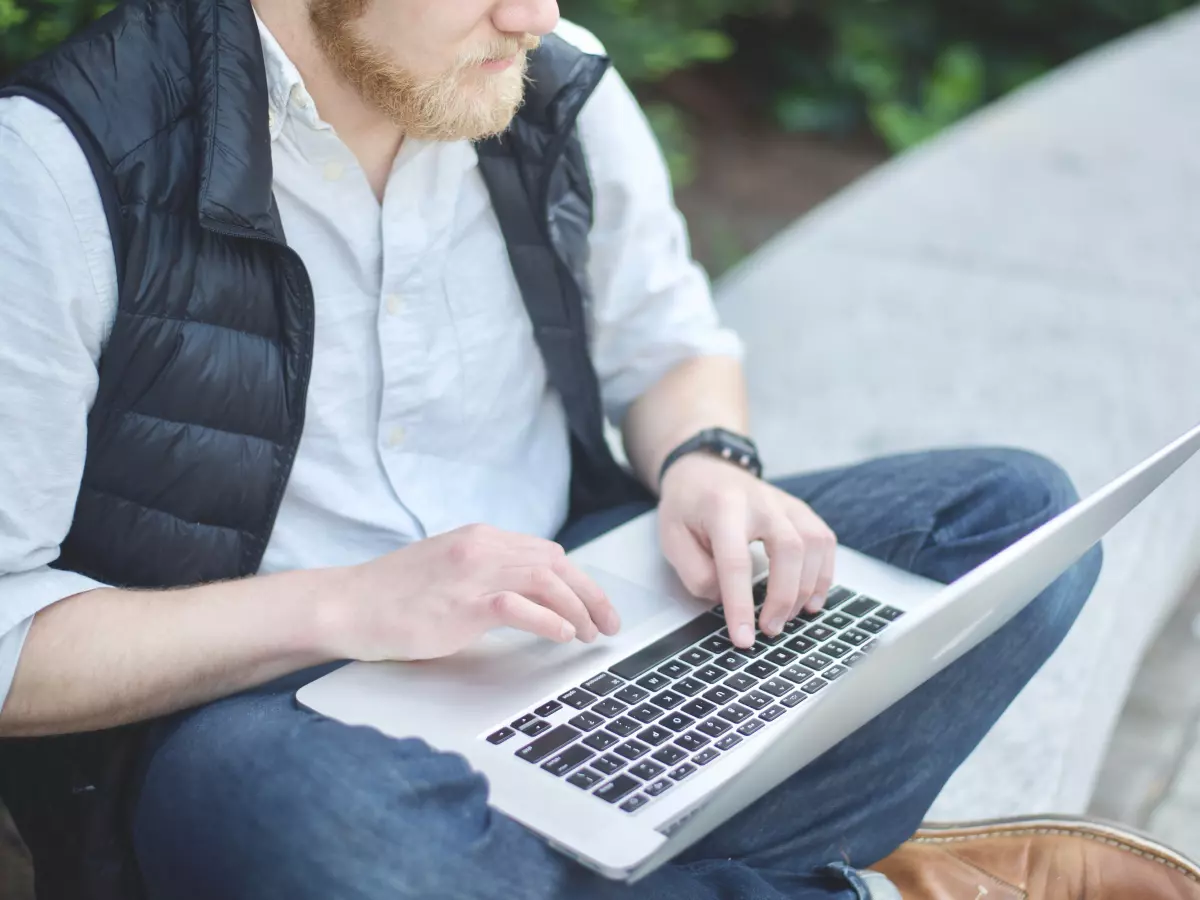 A man sitting on a bench, typing on a laptop.