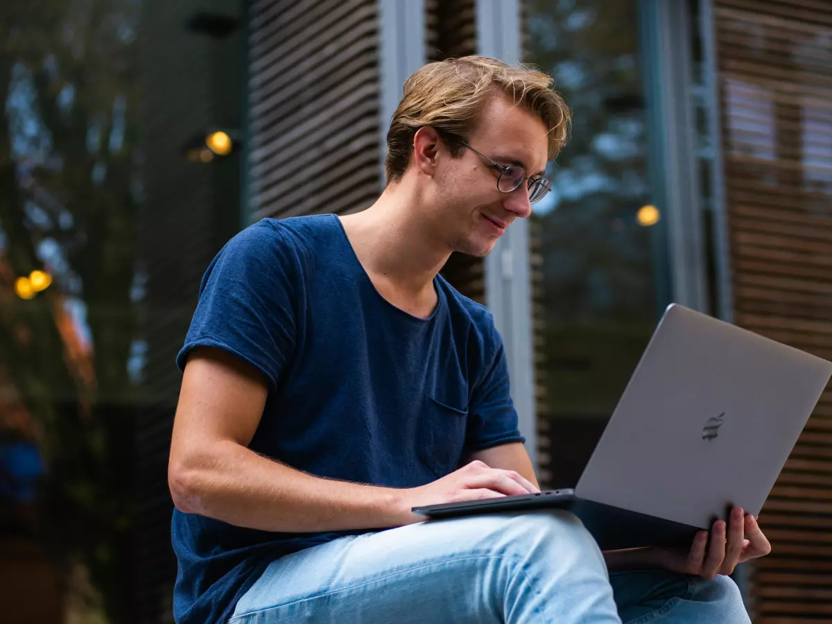 A young man sitting on a step, using a laptop with a serious expression.