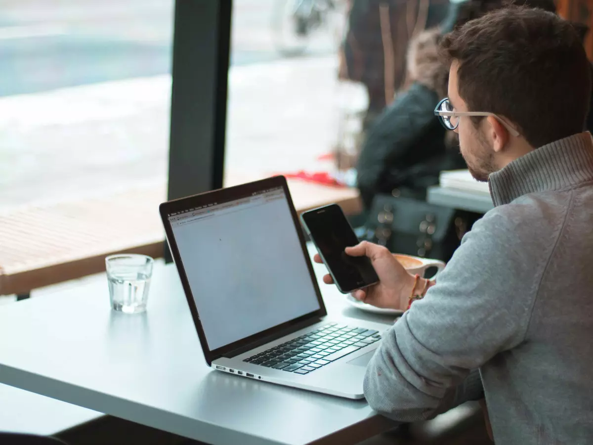 A person sitting in a cafe working on a laptop and holding a smartphone.