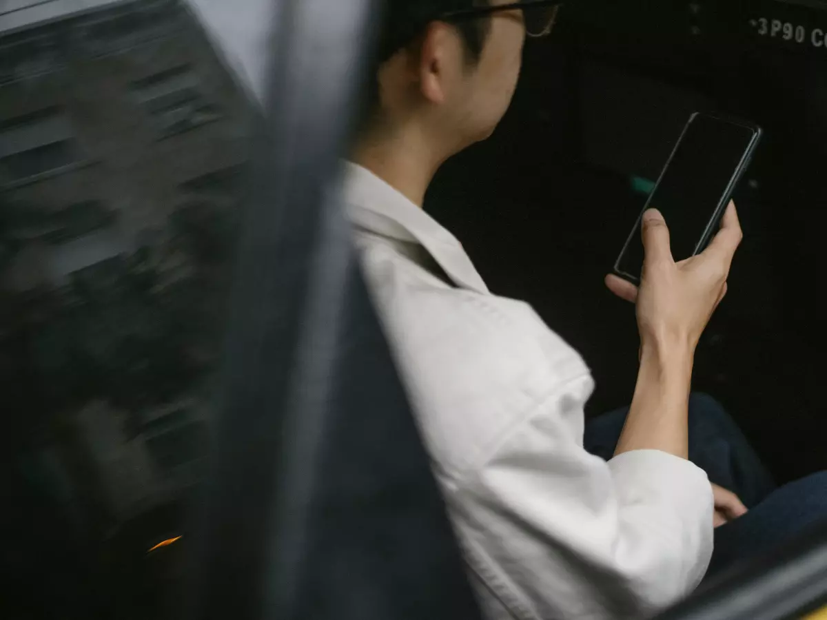 A person using a smartphone in a car, the image is taken from behind the window of the car