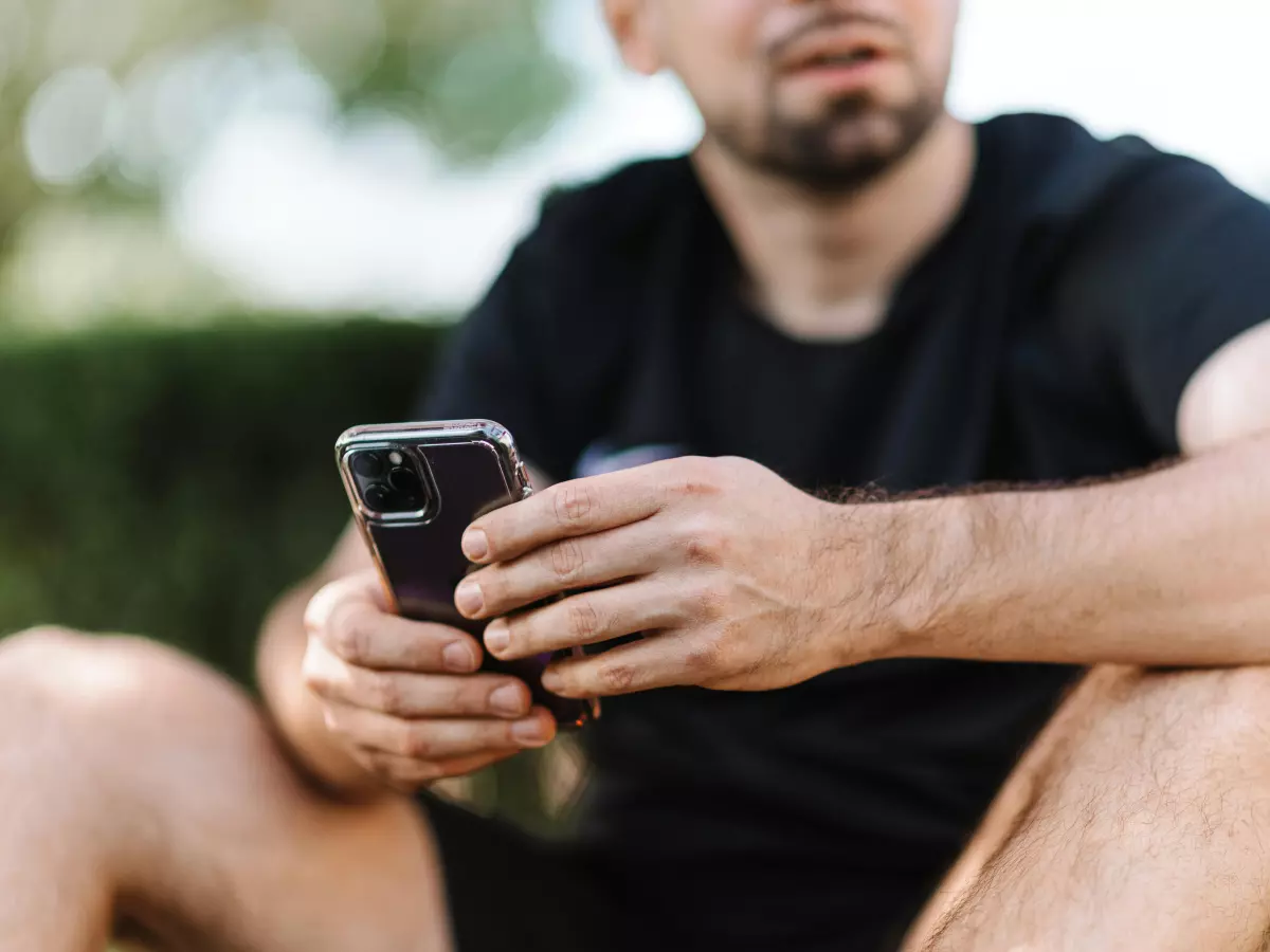 A man sitting on the grass, holding a smartphone.