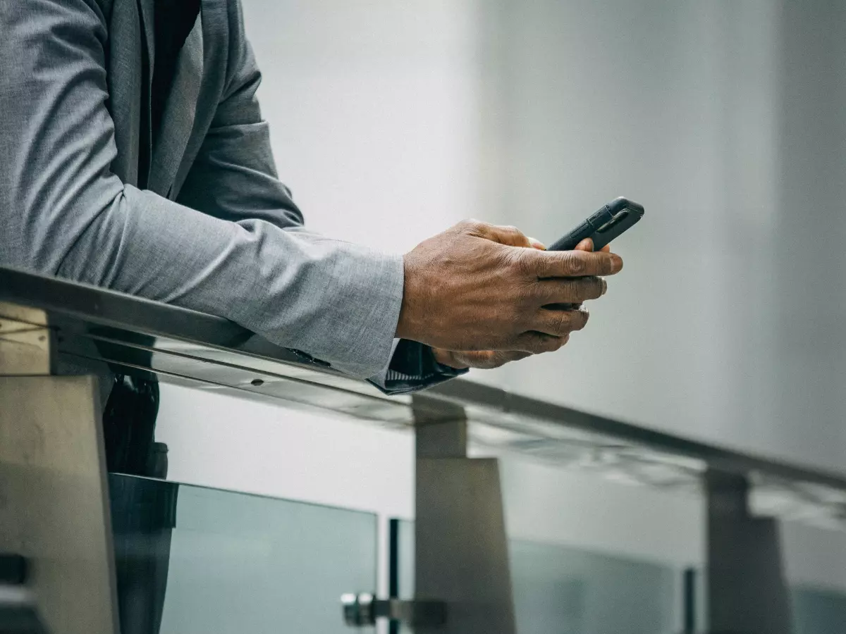 A man in a suit is standing on a balcony and using his smartphone.