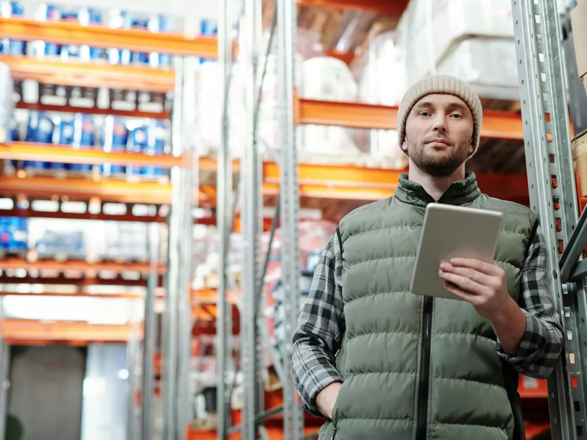 A man in a warehouse aisle holding a tablet in his hand.