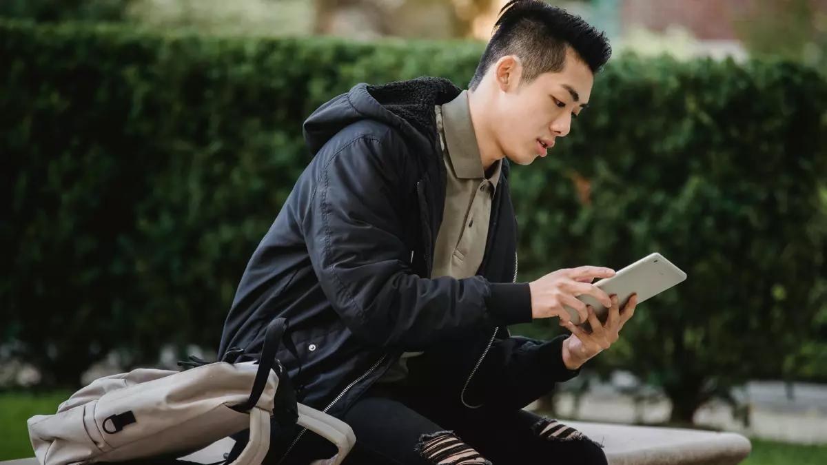 A young man is sitting on a bench and using an iPad.