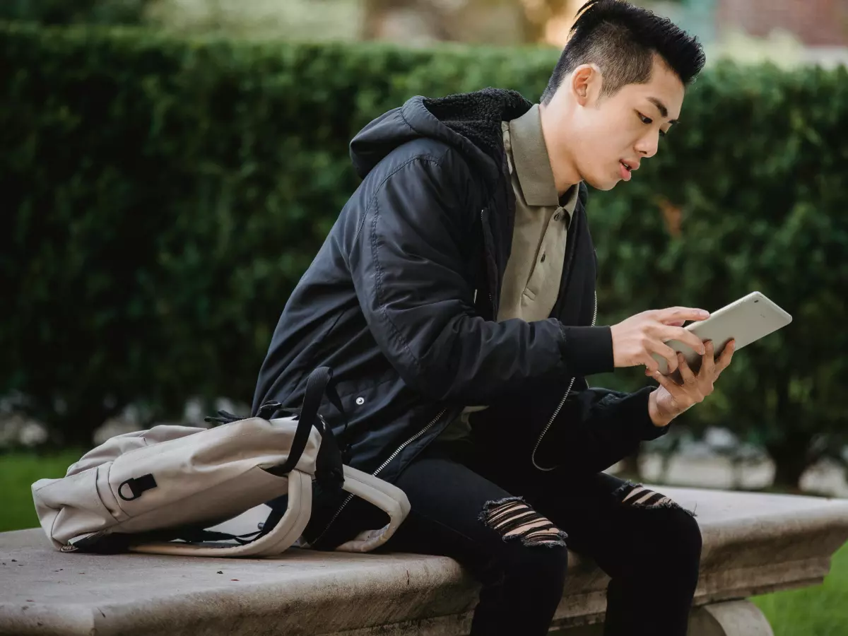 A young man is sitting on a bench and using an iPad.