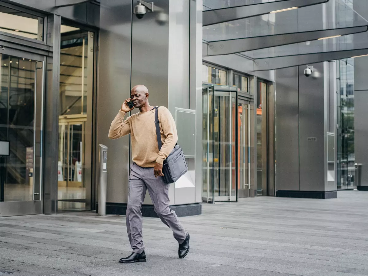 A man in a suit and carrying a bag is walking down a street while talking on a phone.