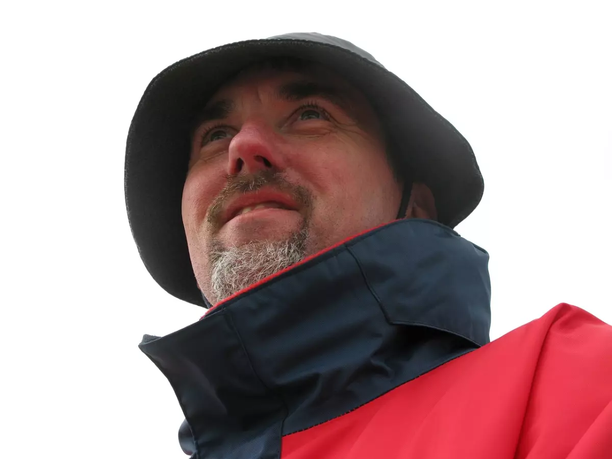 A man with a beard and a hat looking upwards with a thoughtful expression.