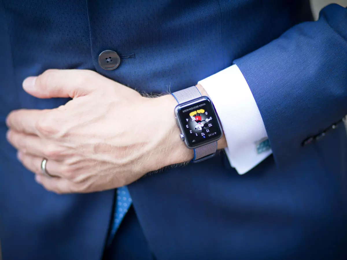 A man wearing a blue suit jacket and white shirt, with a Pixel Watch 3 on his wrist. He has a ring on his finger.