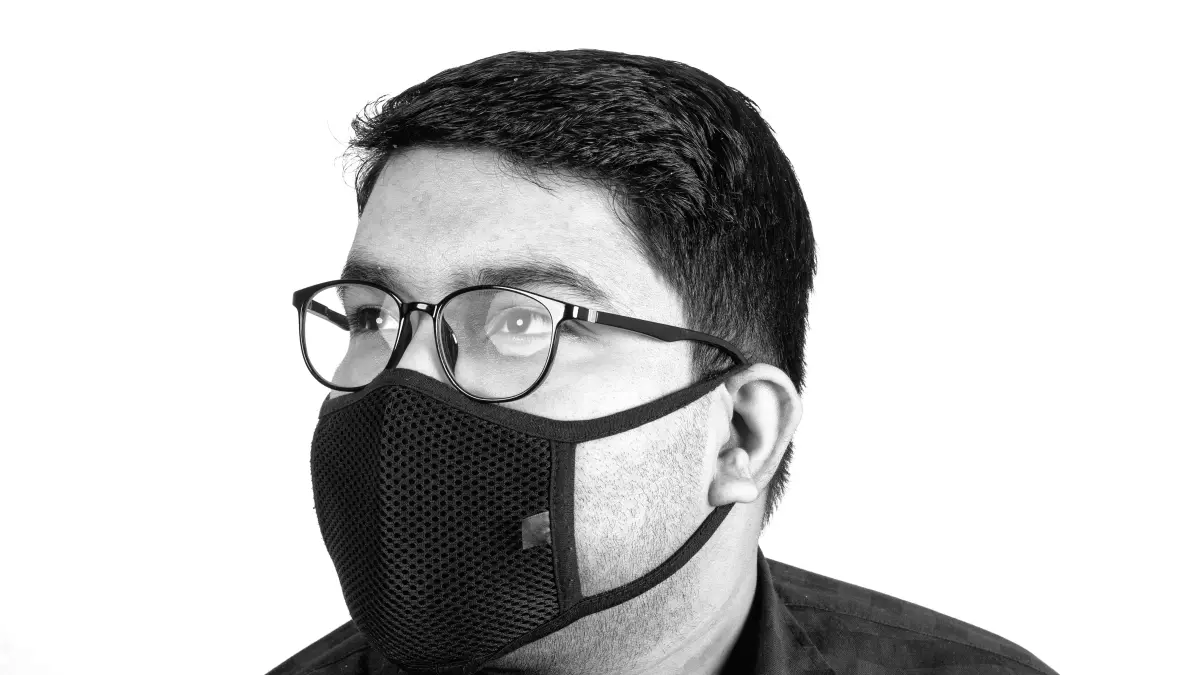 A man wearing glasses and a black face mask, looking off into the distance.