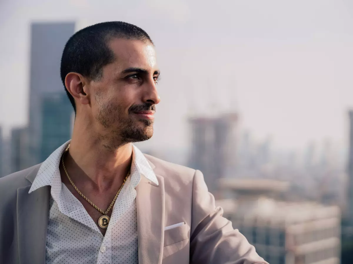 A man in a suit is standing on a rooftop with a cityscape in the background.