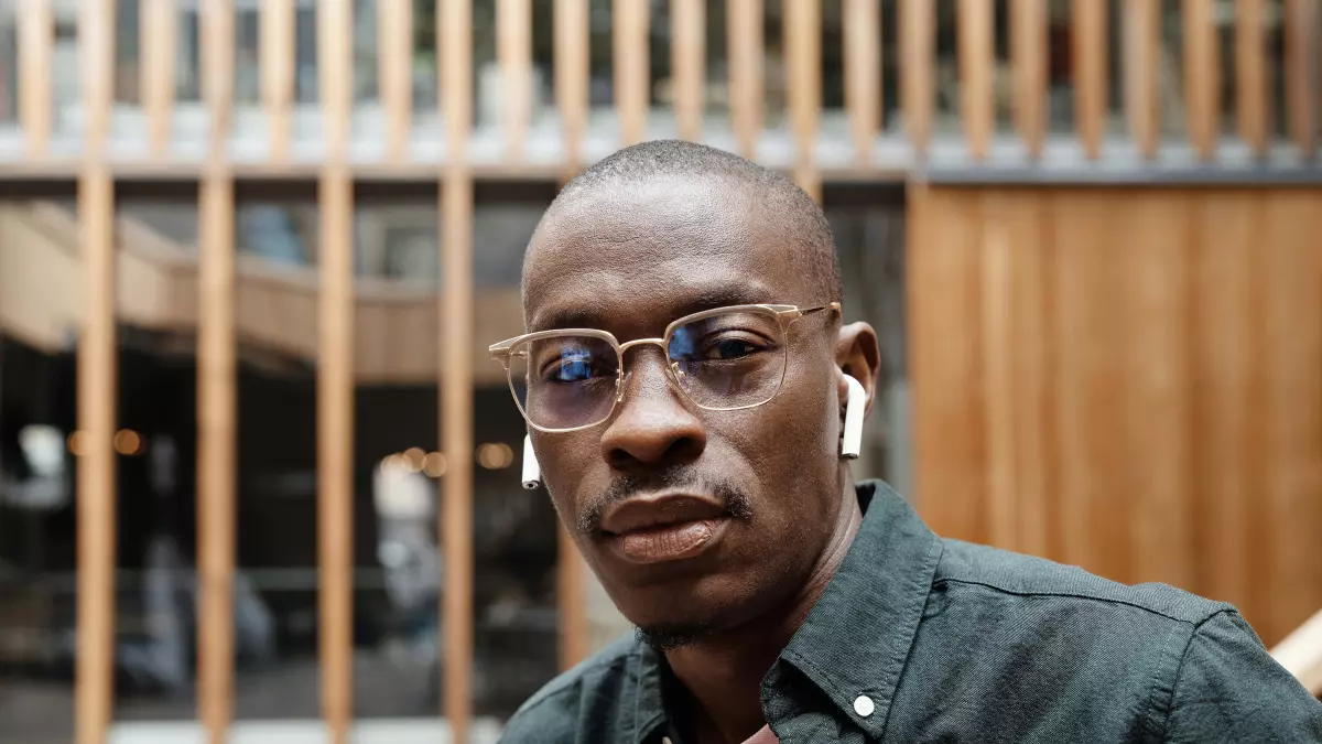 A man wearing glasses is looking at the camera with a serious expression. The glasses have a transparent frame and are made of glass. He is wearing a green shirt.