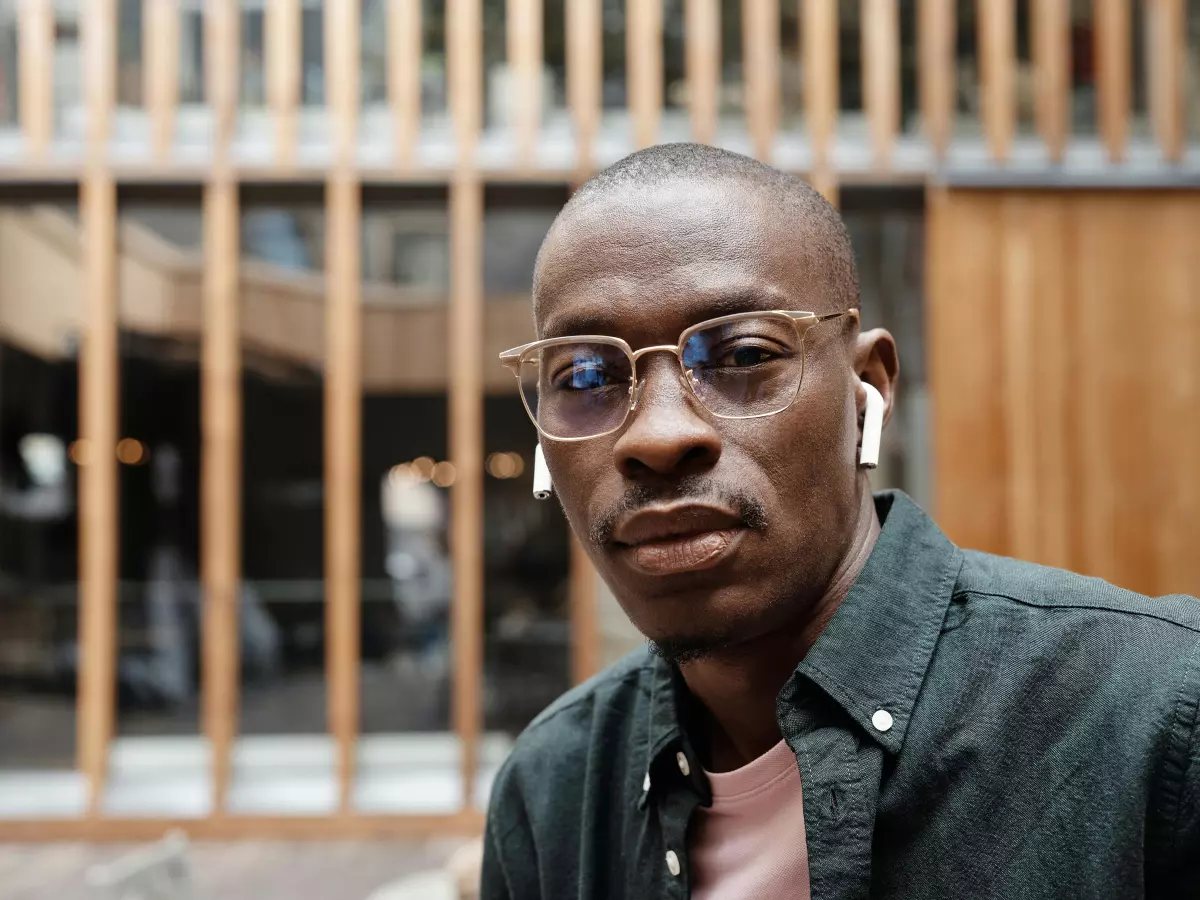 A man wearing glasses is looking at the camera with a serious expression. The glasses have a transparent frame and are made of glass. He is wearing a green shirt.