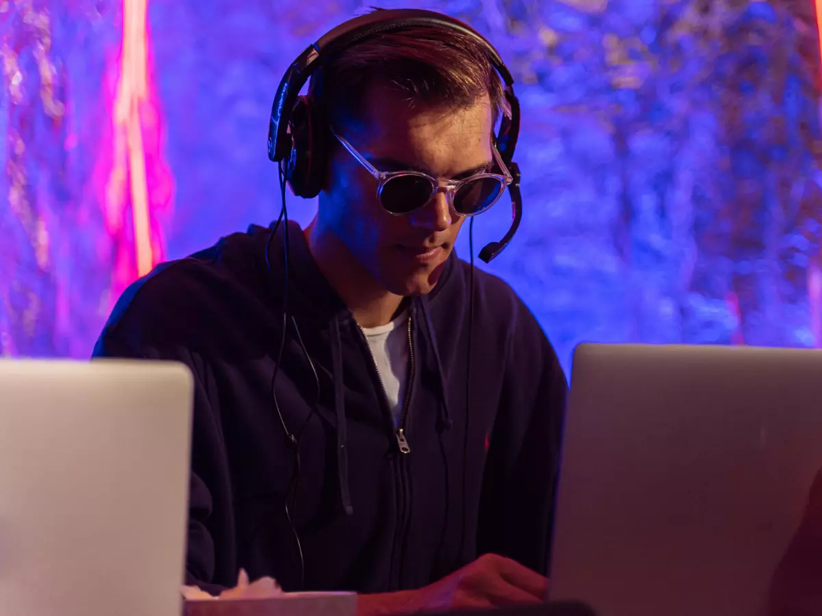 A man wearing a headset is working on a laptop with a colorful background.