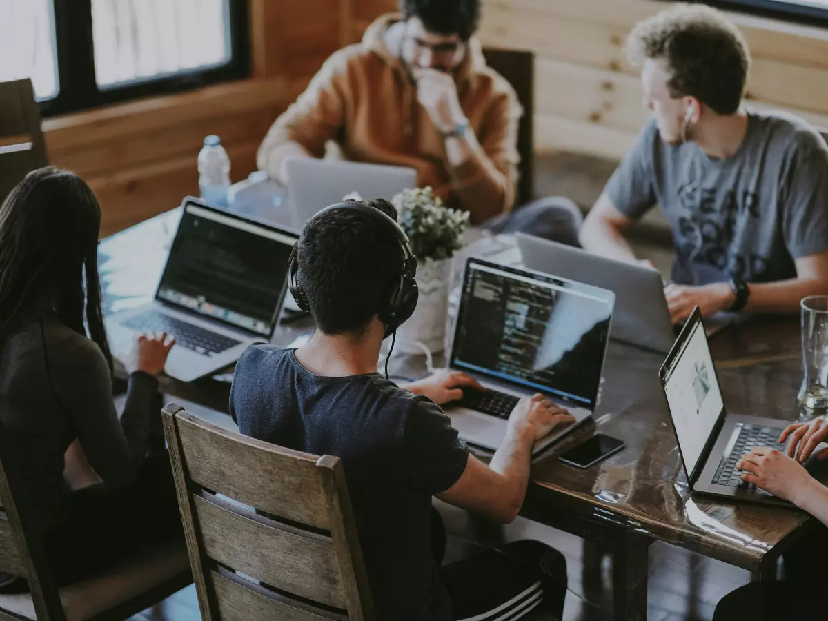 A group of people working on laptops at a table in a modern office space.