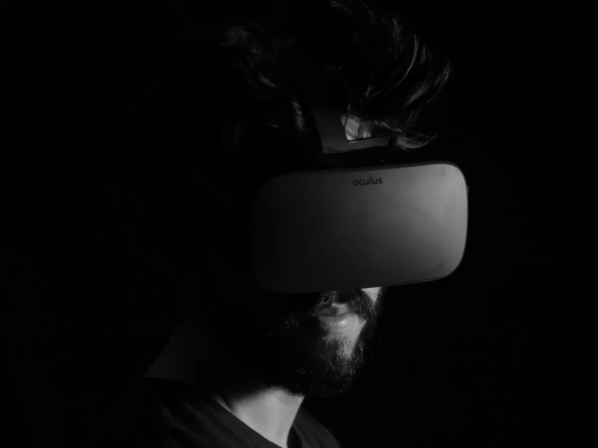 A man wearing VR headset is looking at something in the distance. He is standing in a dark room.