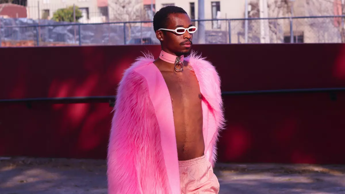 A person wearing a long pink fur coat, walking in a street.