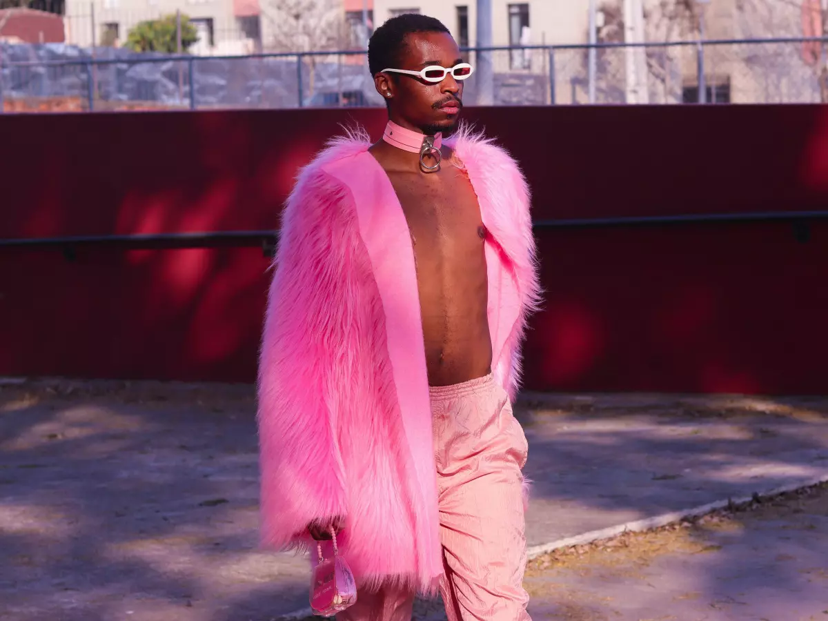 A person wearing a long pink fur coat, walking in a street.