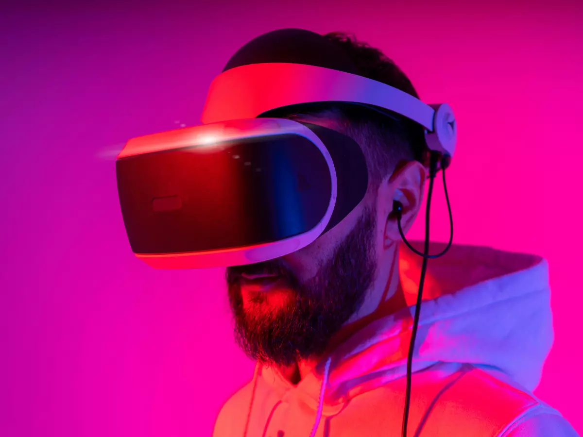 A person wearing a VR headset, with a dramatic lighting effect, in a pink and blue light, standing in a room.  