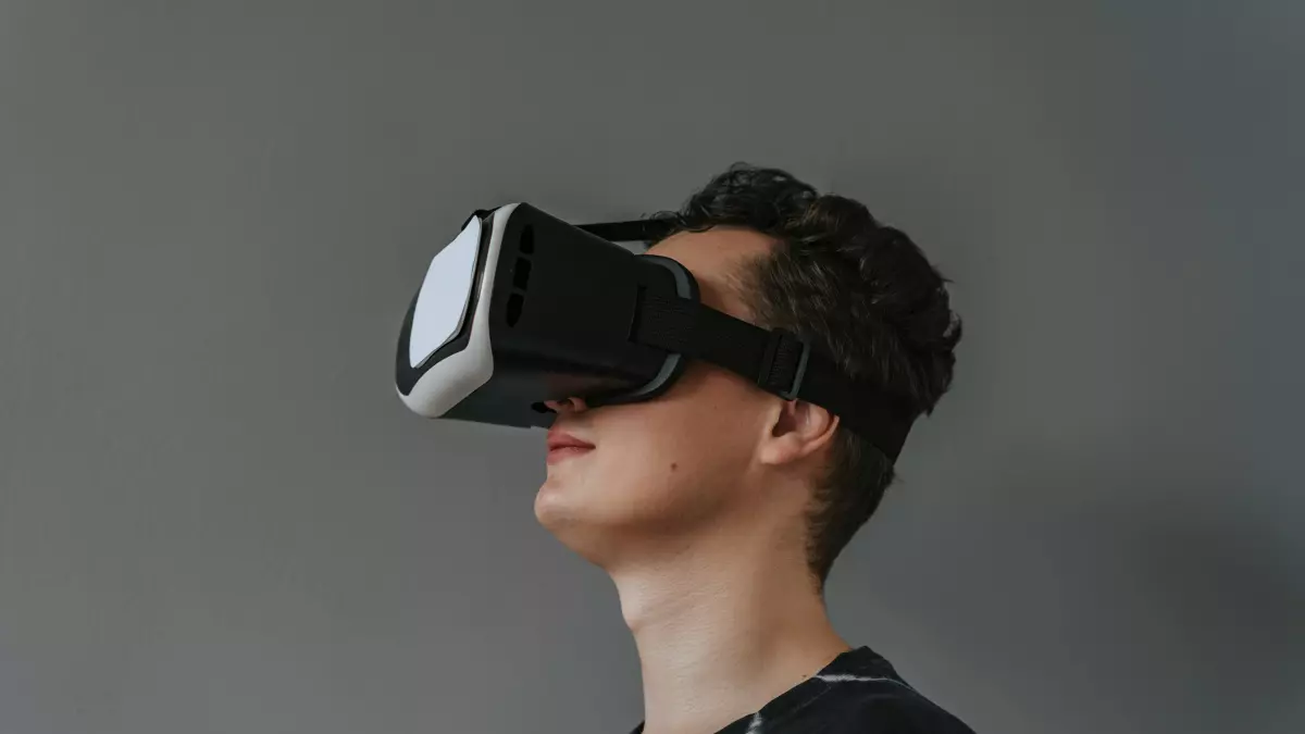 A young man wearing a VR headset looks upwards, with a grey background.