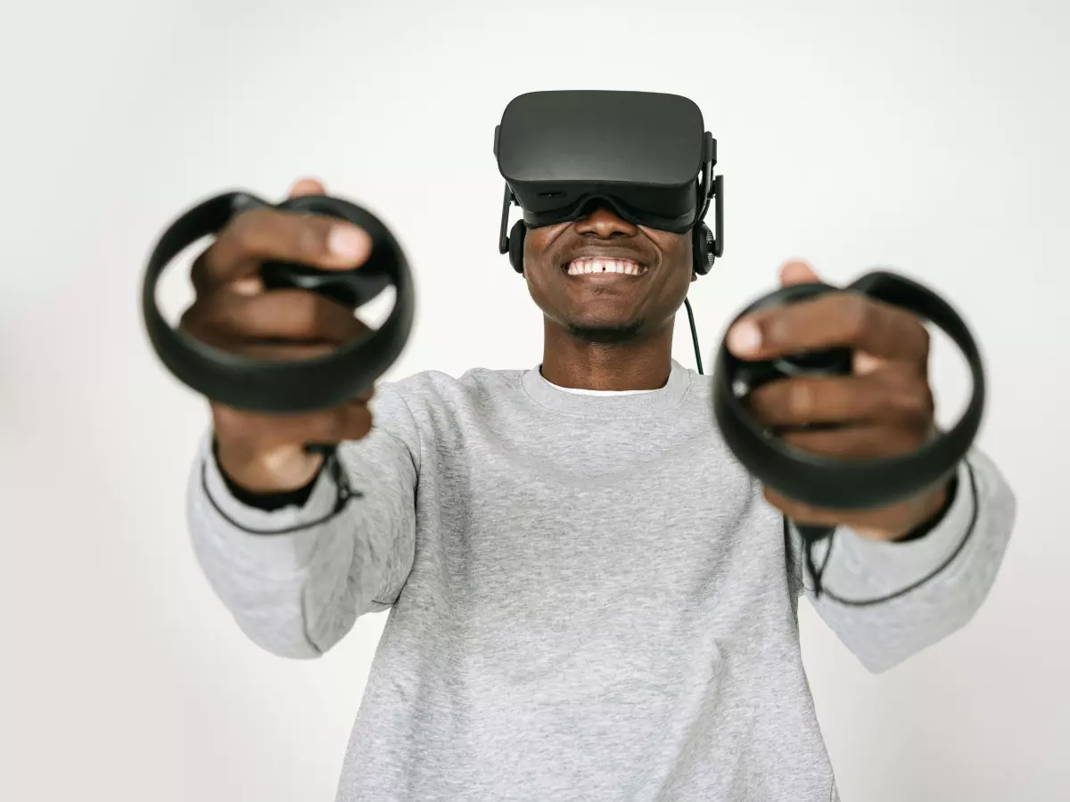 A man wearing a VR headset and headphones while holding VR controllers. He is looking at the camera with a surprised expression.