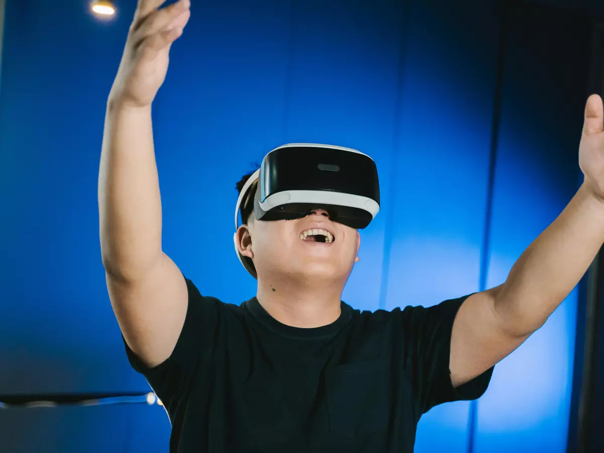 A young man wearing a VR headset with his arms raised in excitement, as if he's experiencing an immersive video game.