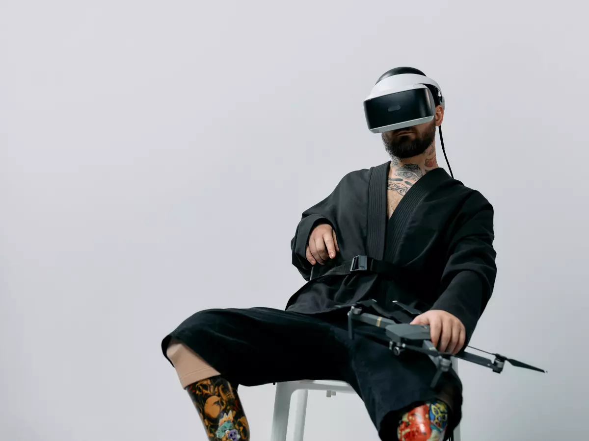 A person wearing a VR headset sits in a chair and controls a drone with a controller.