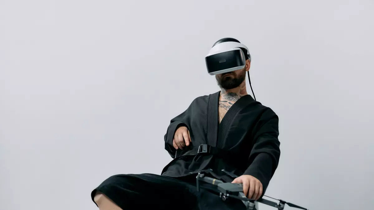 A person wearing a VR headset sits in a chair and controls a drone with a controller.