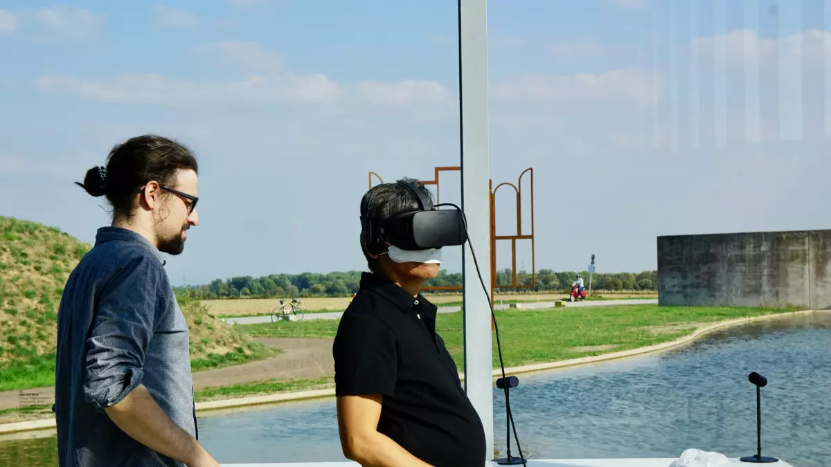 A man wearing a VR headset experiences the virtual world, while another man stands nearby watching.