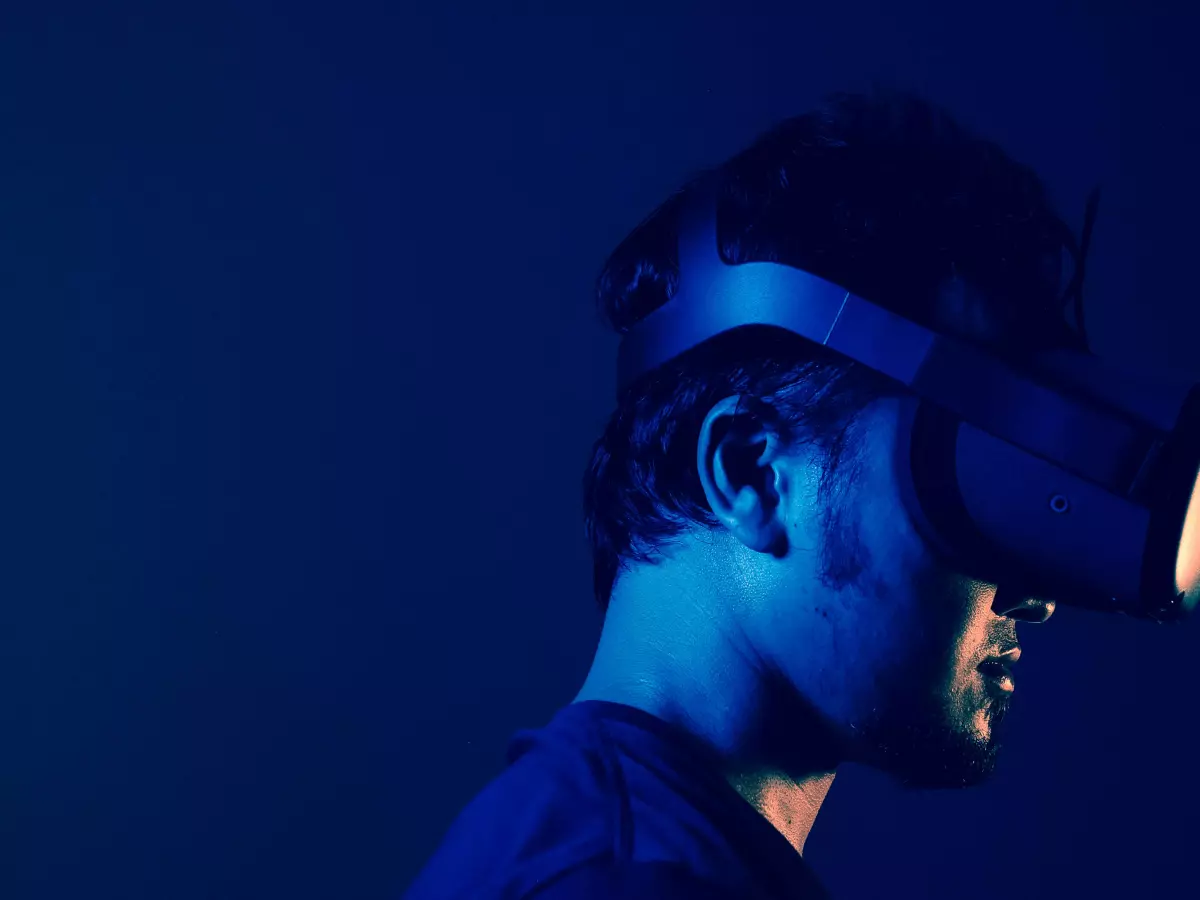 A man wearing a VR headset, looking into the distance, the background is dark blue, the light is coming from the right side.