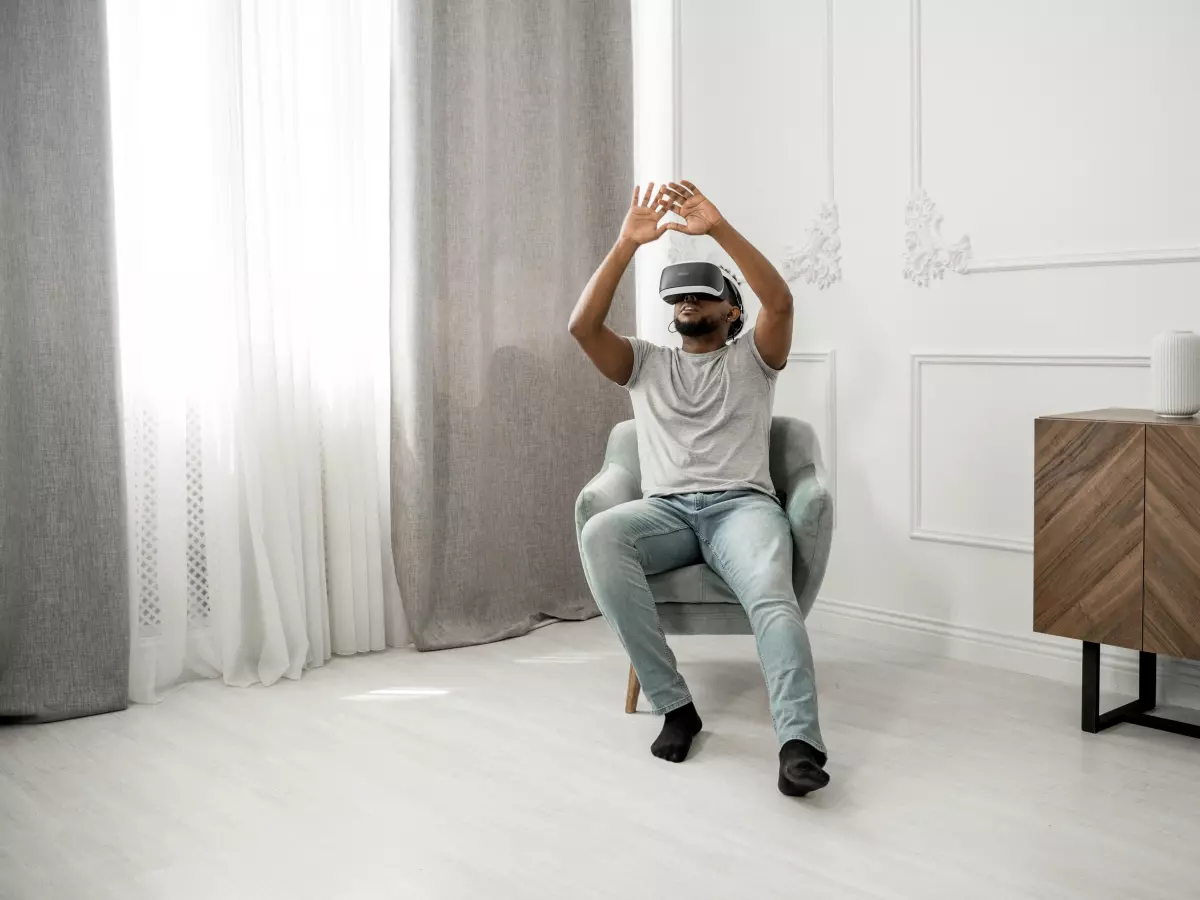 A person wearing a VR headset is sitting on a chair in a living room, looking at something in the virtual world.