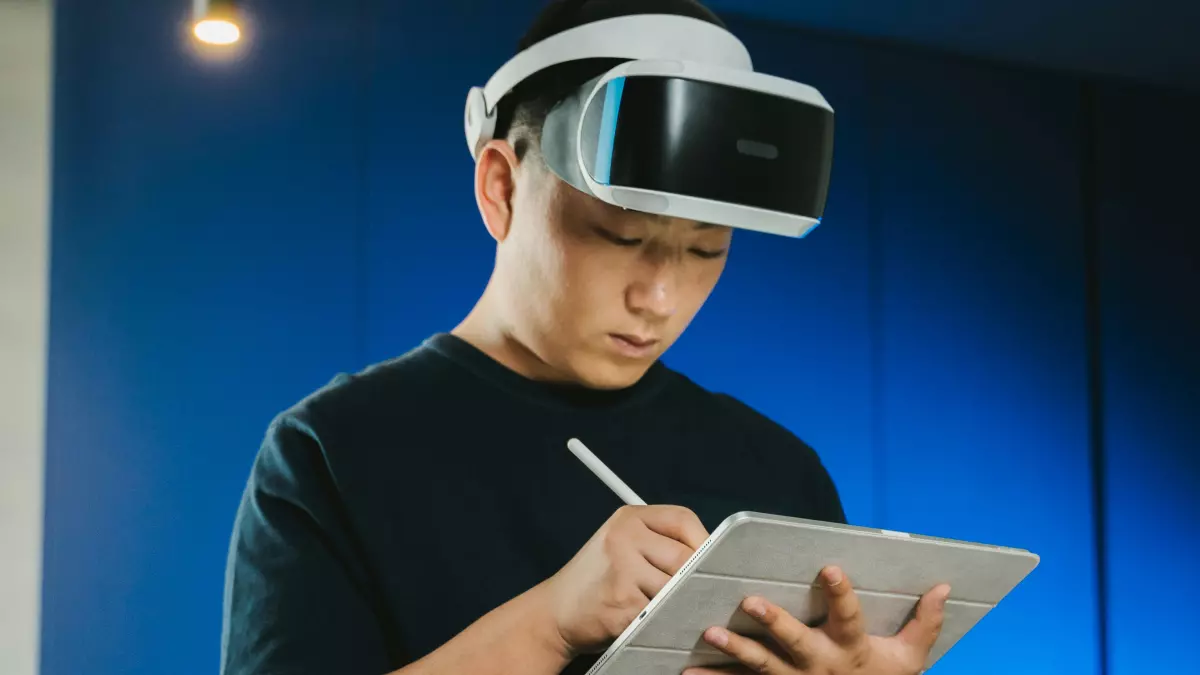 A man wearing AR glasses is drawing on a tablet while standing in front of a blue wall.