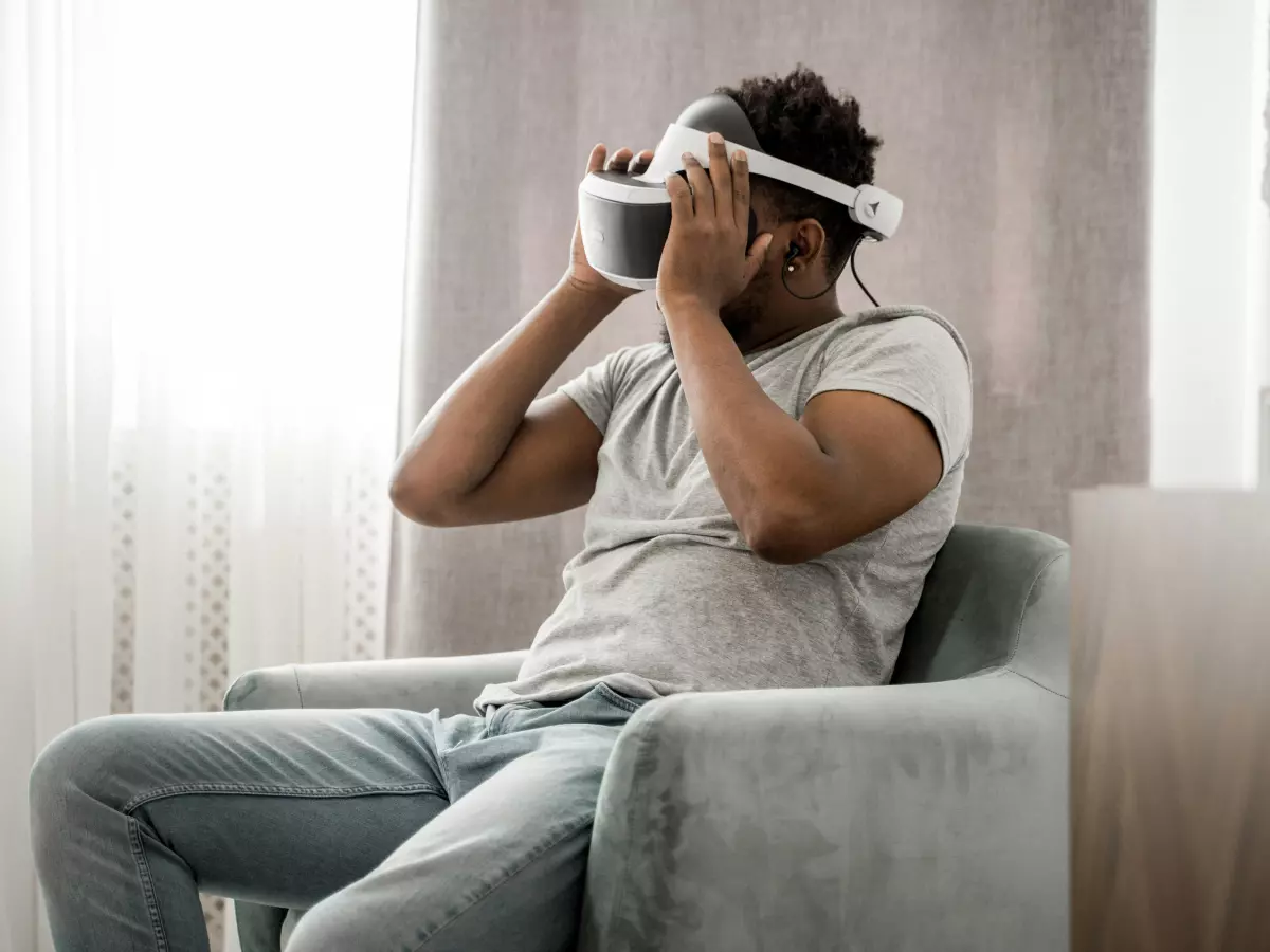 A man wearing a VR headset is sitting in a chair. He is looking at something in the virtual reality world. He seems to be having fun and enjoying the experience.