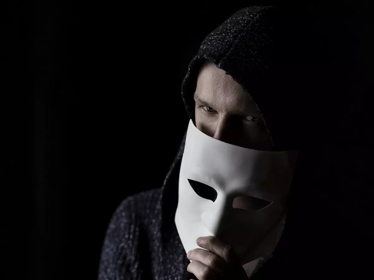 A person in a hoodie wearing a white mask covering their face.